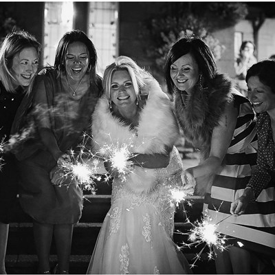 A group of ladies with sparklers around the bride, in black and white
