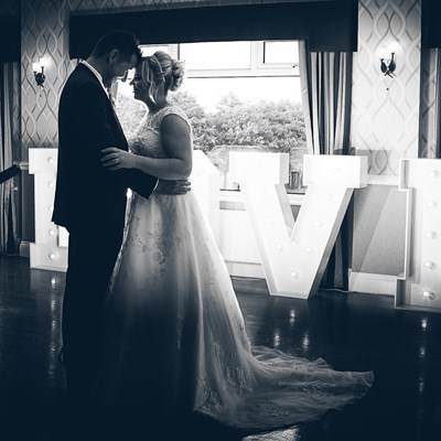Bride & groom on dancefloor with Love letters behind in black and white