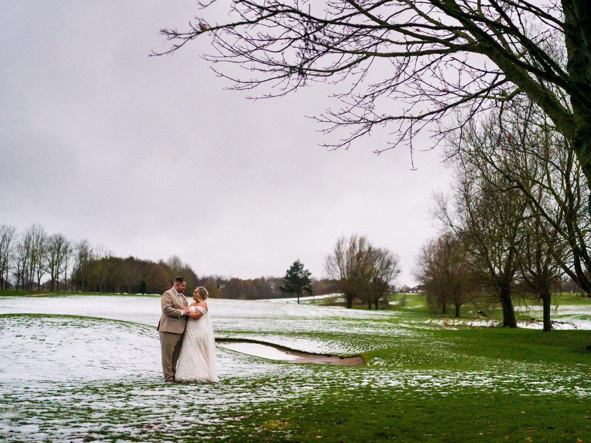A bride and groom embrace on The Manor's golf course, there is snow on the ground.