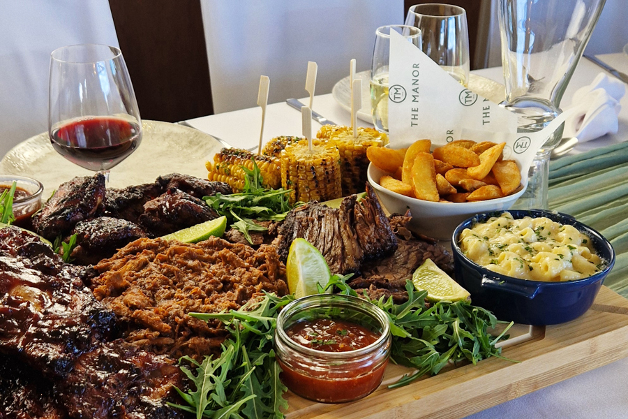 The Grill sharing board at The Manor Leeds; Slow-cooked BBQ Beef Brisket, Sticky BBQ Chicken Thighs, Pulled Pork with Smoky Glaze, Pork Ribs, Corn on the Cob, Mac & Cheese, Skin-on Wedges, Classic Crunch Slaw and Tomato & Cucumber Salad.