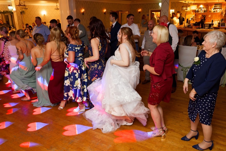 A bride dancing in a line with her female guests on the dancefloor in The Manor Leeds.