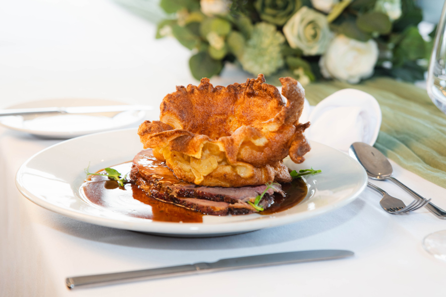 Roast beef on a plate, with Yorkshire Pudding and gravy placed on a formal dining table.