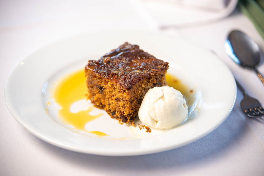 Sticky toffee pudding with ice cream and sauce, placed on a formal dining table.