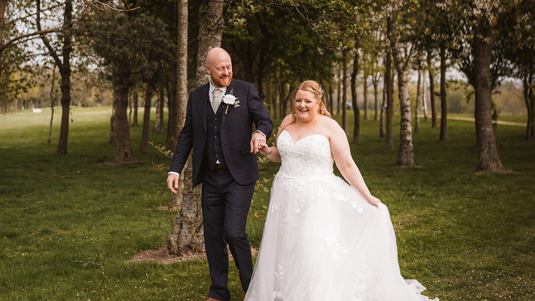 A bride and groom walk hand-in-hand through trees at The Manor Leeds.