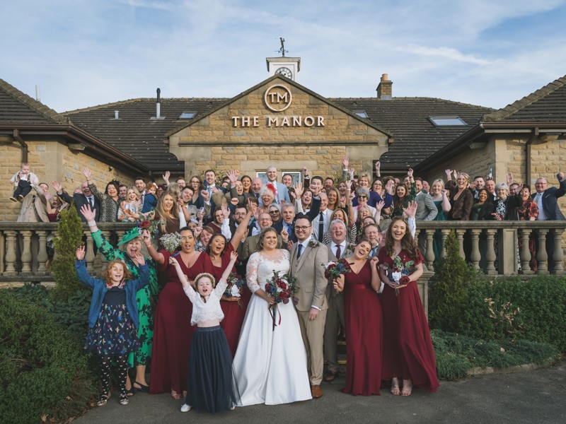 A bride and groom with their guests at the front of The Manor building.