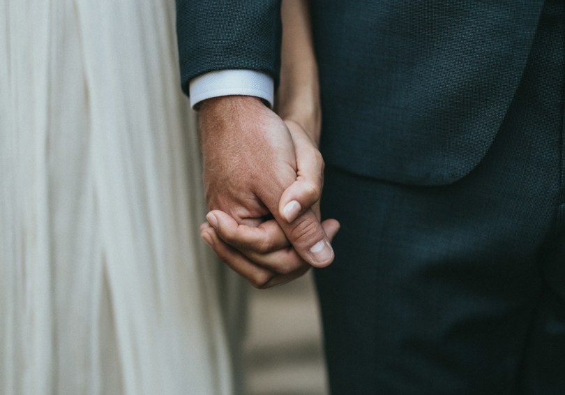 A close shot of  bride and groom holding hands.