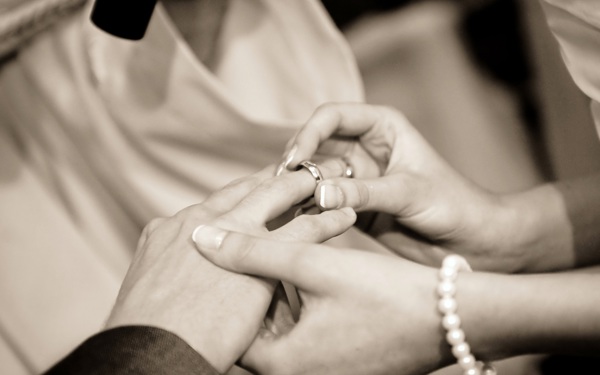 A sepia photo of a female hand placing a wedding ring on a male hand.