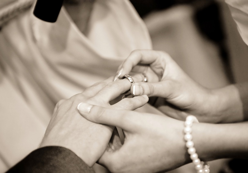 A sepia photo of a female hand placing a wedding ring on a male hand.