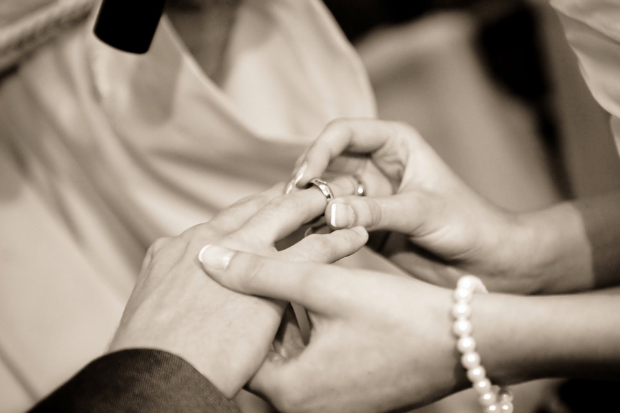 A sepia photo of a female hand placing a wedding ring on a male hand.