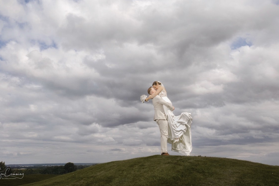 A groom lifts his bride beneath a moody sky at The Manor Leeds.