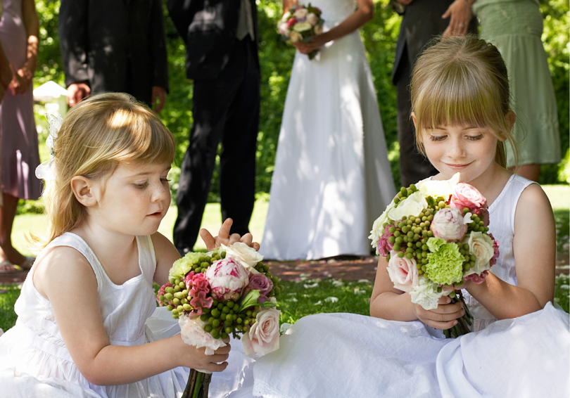 Two young bridesmaids in white dresses sitting down admiring their flower posies.