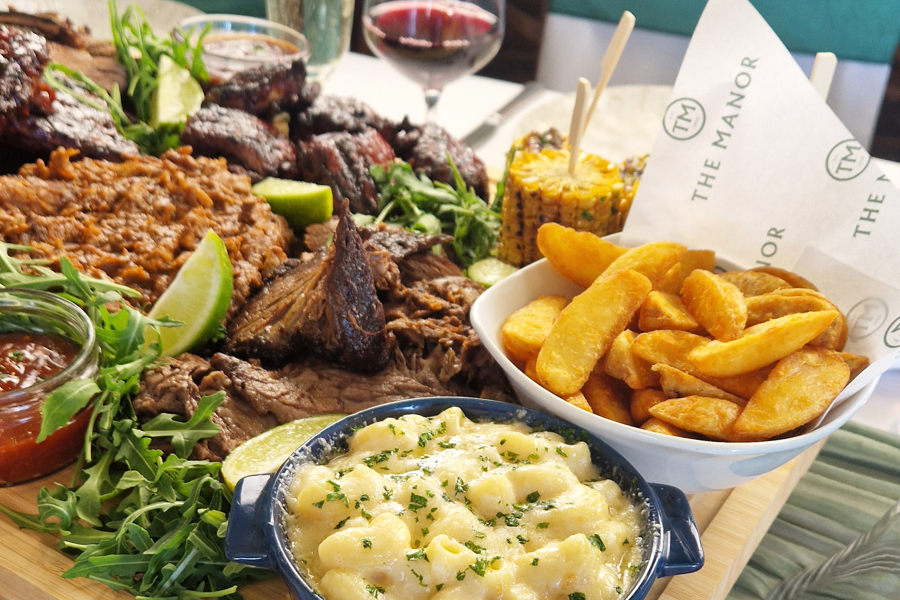 The Grill sharing board at The Manor Leeds; Slow-cooked BBQ Beef Brisket, Sticky BBQ Chicken Thighs, Pulled Pork with Smoky Glaze, Pork Ribs, Corn on the Cob, Mac & Cheese, Skin-on Wedges, Classic Crunch Slaw and Tomato & Cucumber Salad.
