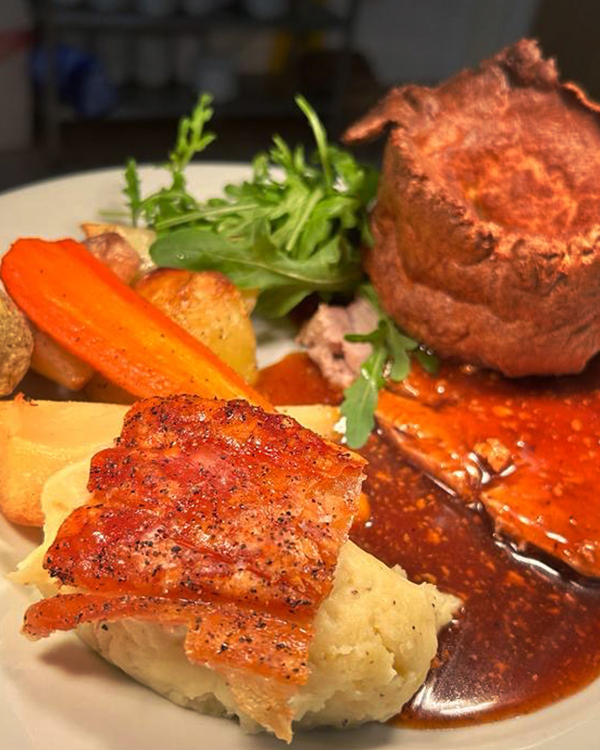 Roast dinner on a plate, Yorkshire Pudding, pork crackling, mashed potato and gravy.