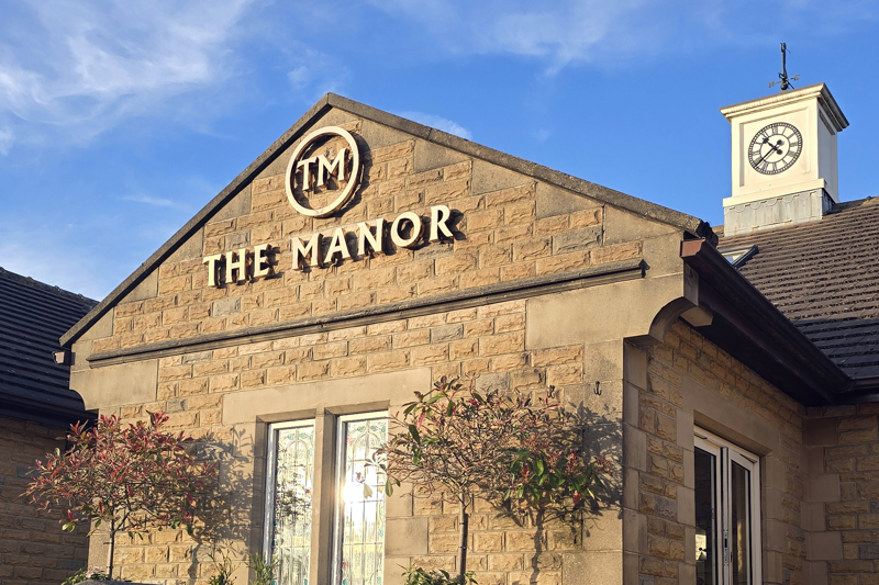 The main entrance of The Manor, showing the clocktower and the gold logo.
