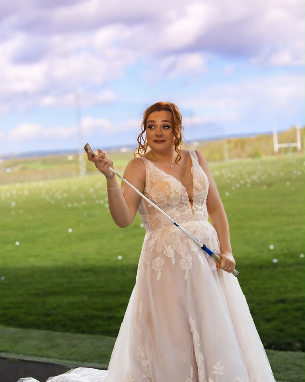 A bride stands in The Manor's driving range holding a golf club.