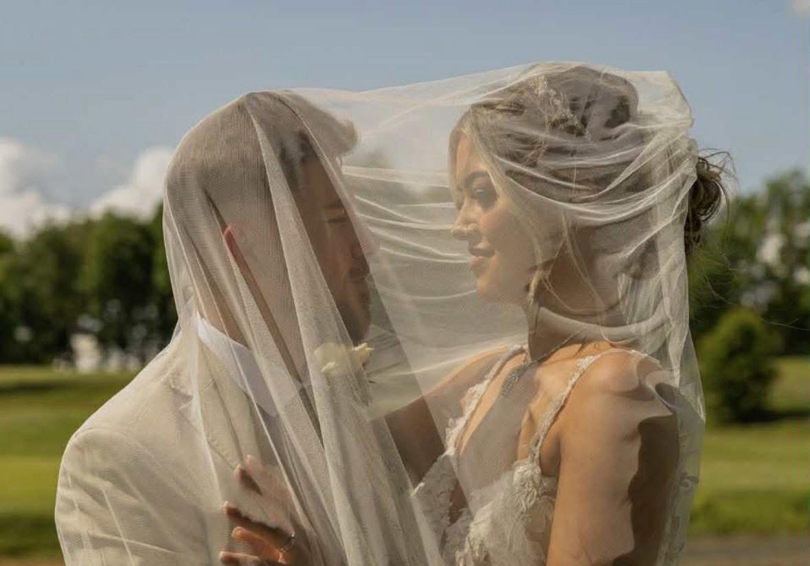 A bride and groom embrace under her veil at The Manor's lake.