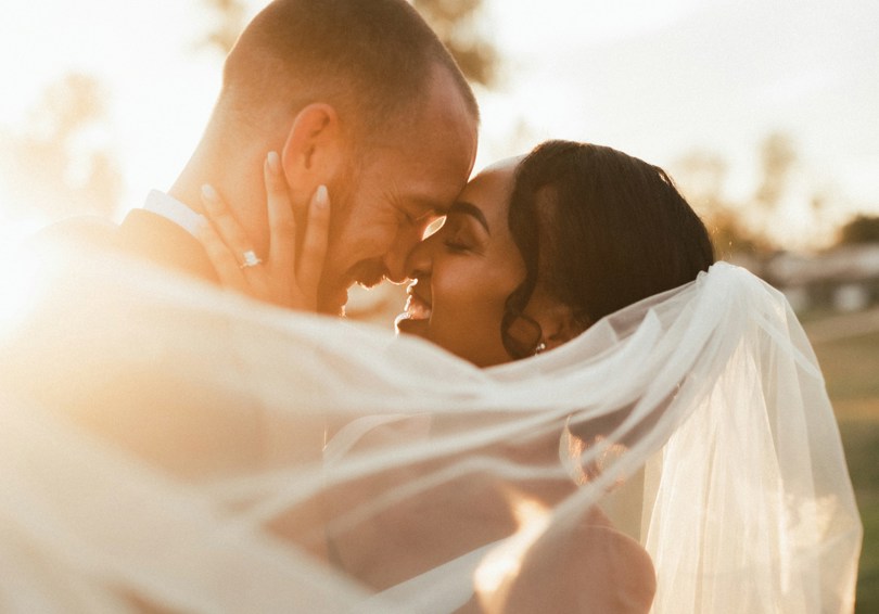 A bride and groom embracing at sunset.