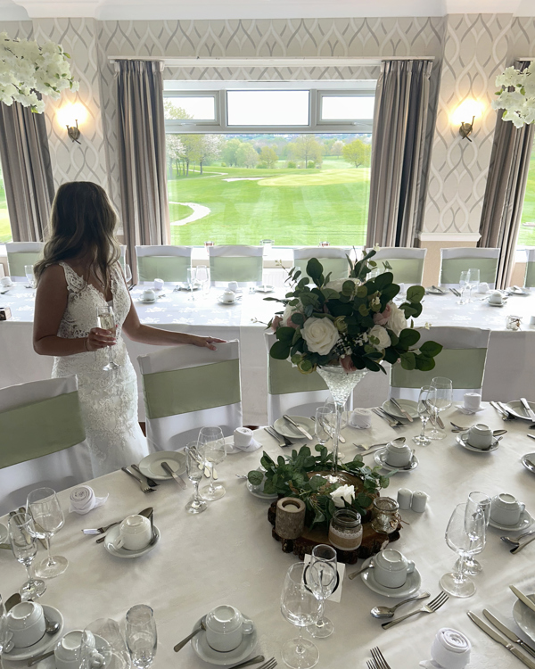 A bride looking out at the view over The Manor golf course, standing beside a table set for a wedding breakfast.