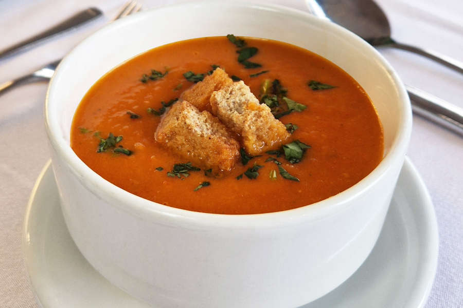 A bowl of tomato soup with croutons placed on a formal dining table.
