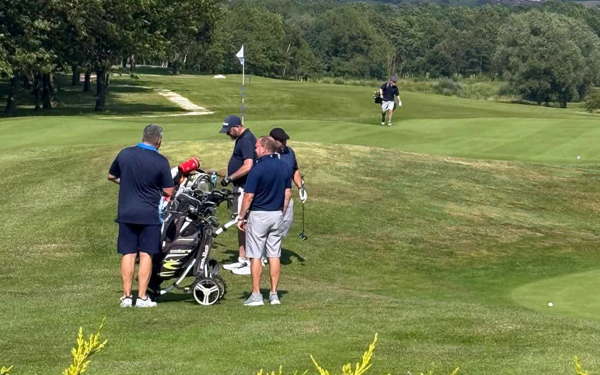 A group of four golfers standing beside the 18th green at The Manor Leeds.