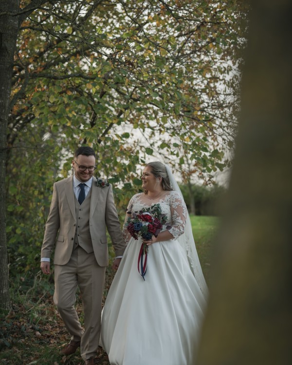 A bride and groom walk hand-in-hand through trees at The Manor Leeds.
